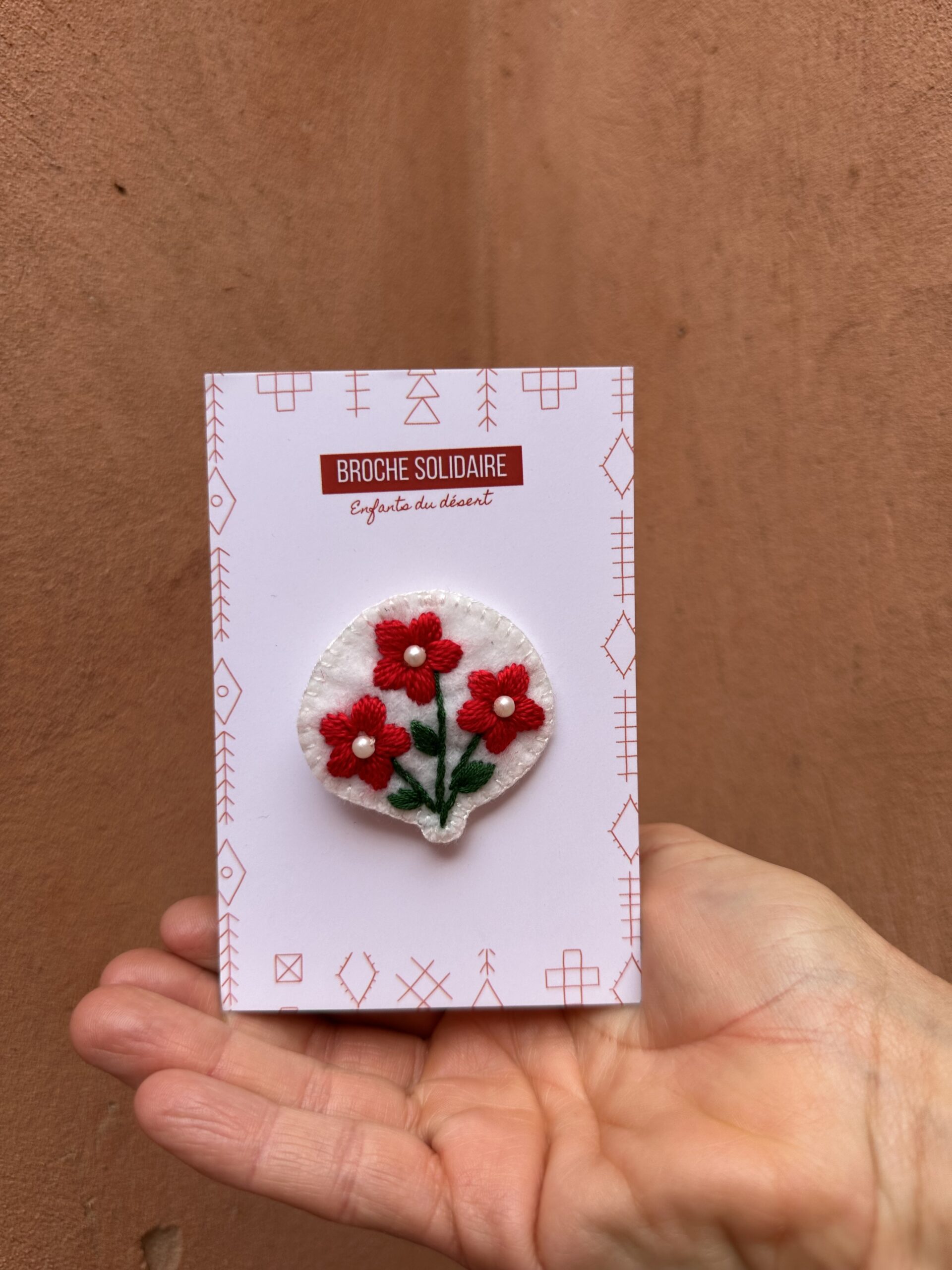 Broche en feutrine blanche avec des fleurs rouges.