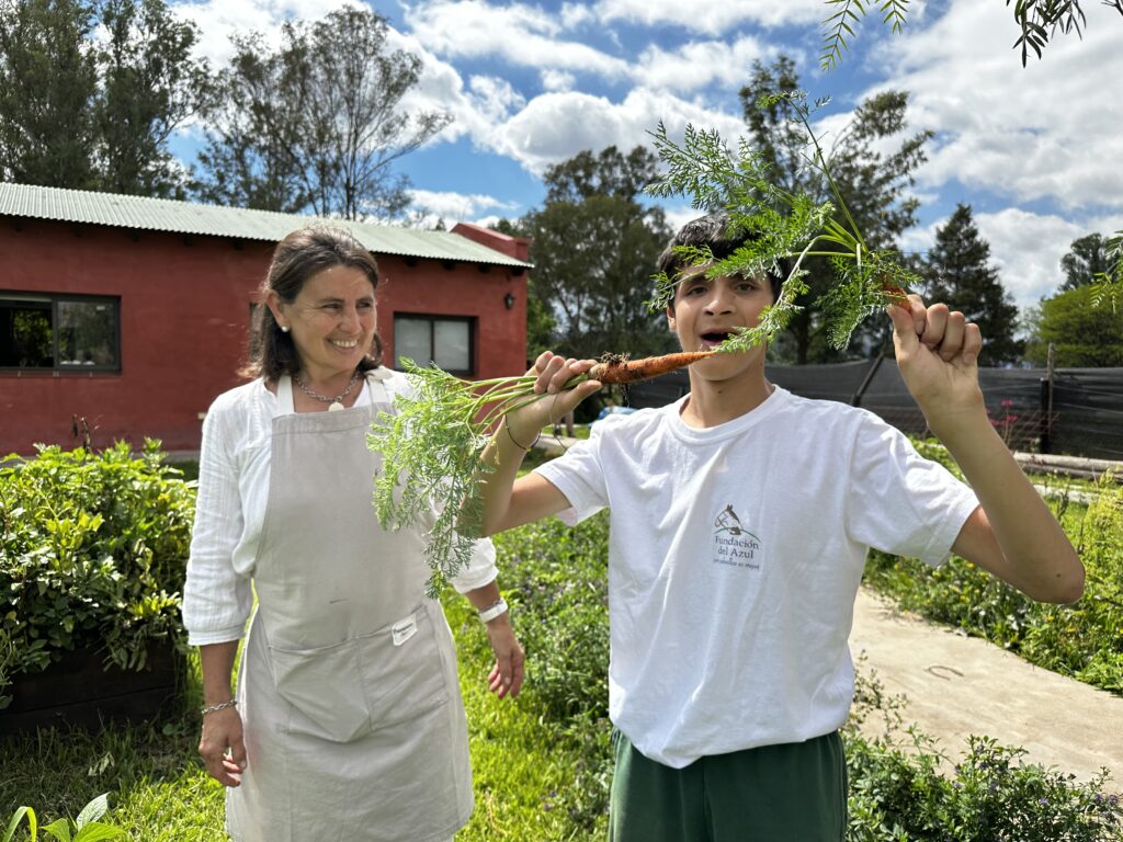 jeune garçon montre des carottes issues du potager, regardé en souriant par professeure de jardinage